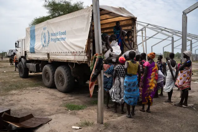 Women from Murle ethnic group unload bags of sorghum from a truck during a food distribution by United Nations World Food Programme (WFP) in Gumuruk, South Sudan, on June 10, 2021,