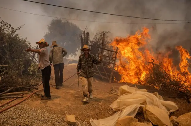 Locals try to extinguish small fires in a village near a wild forest fire in Morocco's northern region of Ksar Sghir on July 14, 2022.