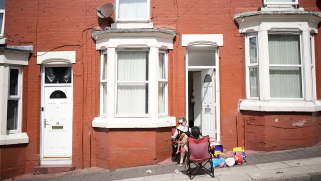 Family sitting outside a terrace house to keep cool