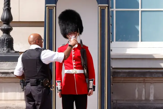 A member of the Queen's Guard receives water to drink outside Buckingham Palace in London