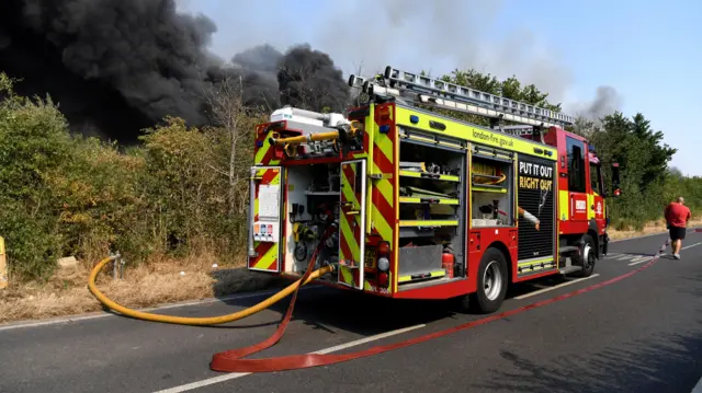 A firefighters truck is parked near a fire that burns during a heatwave in east London