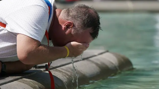 A person wets their face in a fountain at Trafalgar Square in central London.