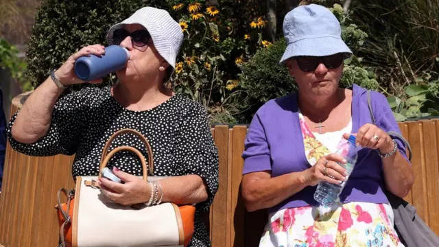 Two women drinking water on a bench during the heatwave