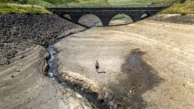 A person walks on the dry bed of a tributary to the Dowry Reservoir close to Oldham