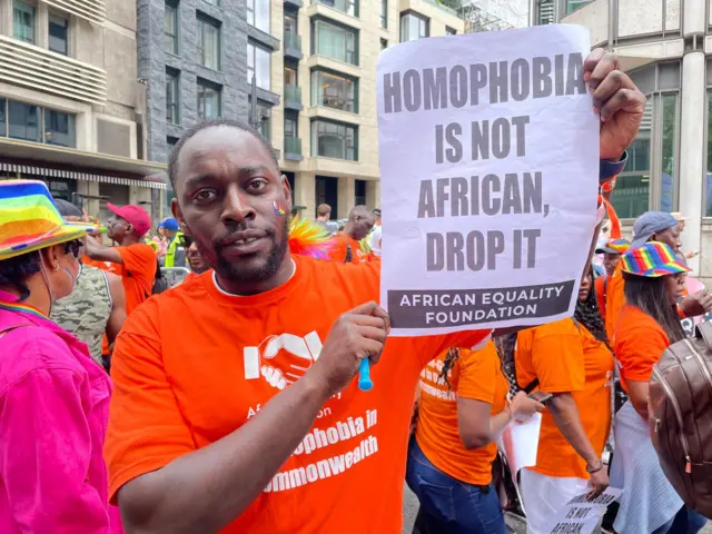 Kevin from Uganda holding a sign that says 'homophobia is not African, drop it'