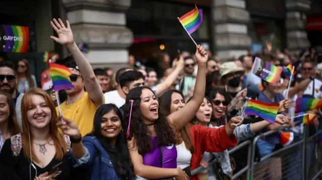 People wave rainbow flags as they watch the 2022 Pride Parade in London