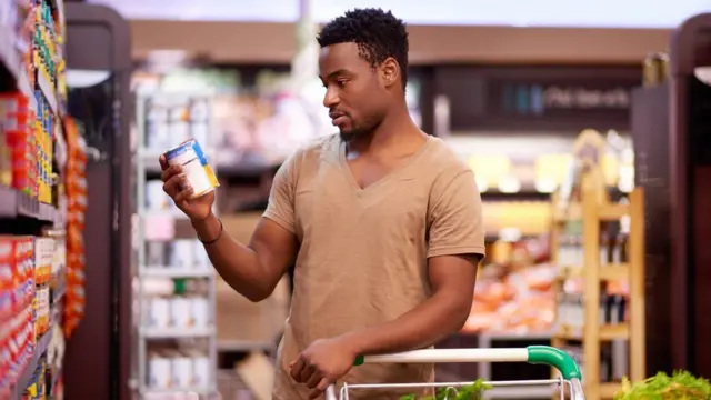 A man looks at a caned product in a supermarket