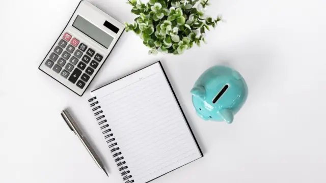 A calculator, notepad, pen and piggy bank