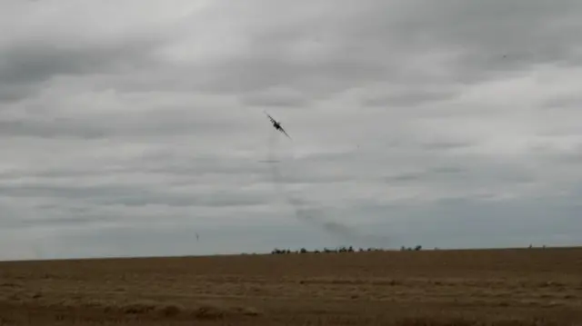 a jet flies low over the fields