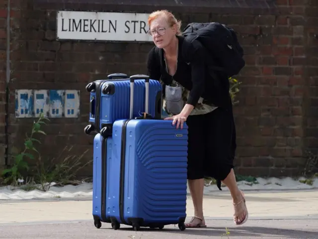 A woman wheels her suitcase down the motorway to beat the traffic jam