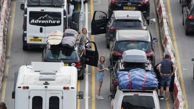 people getting out of their cars as they queue for hours