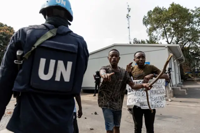 UN soldier is seen as demonstrators carry a poster against the peacekeeping mission in the Democratic Republic of Congo  at the UN facilities in Goma on July 25, 2022