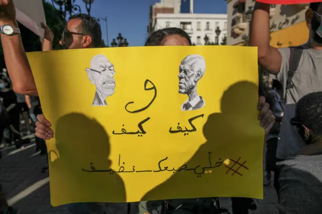 A Tunisian protester holds up a caricature of Tunisian President Kais Saied looking at Rached Ghannouchi the president of the islamist Ennahda party