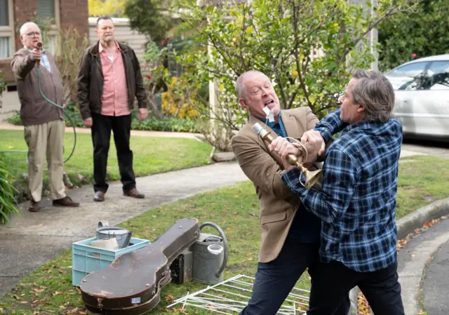 Harold stands in the background with a hose pointed at Clive and Mike, who are fighting with the remains of a lamp