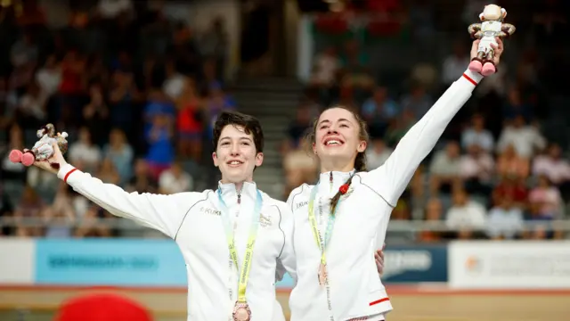 Sophie Unwin and Georgia Holt celebrate with borrowed bronze medals on the podium at the Commonwealth Games