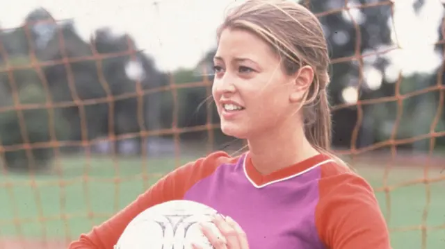 Holly Valance, as character Felicity Scully, stands in a goal and holds a football