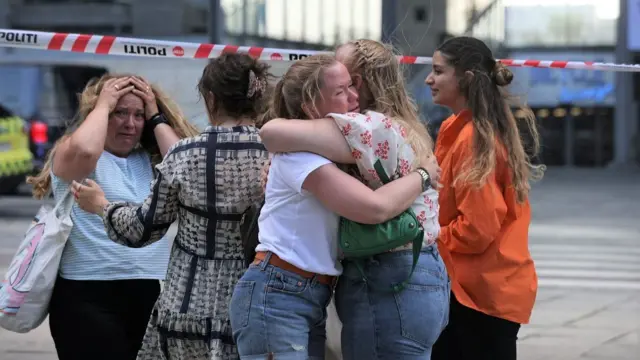 Distressed women hug and another holds her head in her hands outside the shopping centre