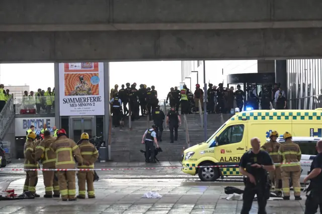 Firefighters, armed police and other emergency services gather outside the shopping centre, alongside an ambulance and police cordon