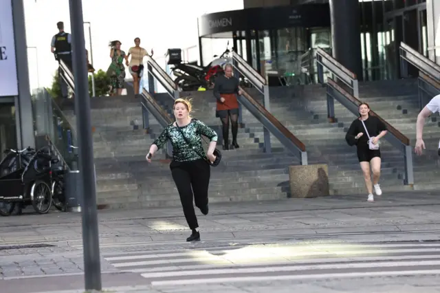 A woman in the foreground runs outside the shopping centre, as others behind her flee down the steps