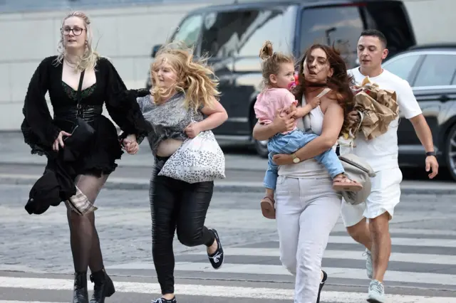 People out shopping flee across the road with their children