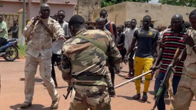 A soldier points a rifle at a man suspected of taking part in thwarted "terrorist" attack as he lies motionless on the floor after being beaten by a crowd, in front of the military base in Kati, Mali - July 2022