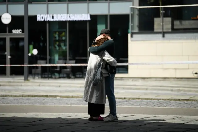 A woman and man hug next to the Field's shopping centre, a day after the shooting at the mall