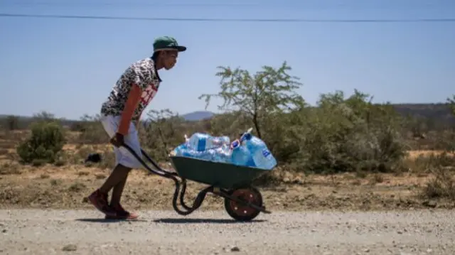 A young man pushes a wheelbarrow containing refilled bottles of water