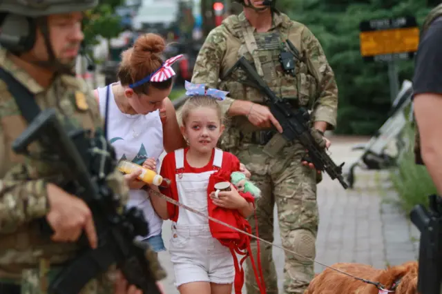 Armed police escort a family away from the scene of a shooting in Highland Park, 4 July 2022