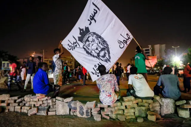 People gather by a make-shift barrier made of bricks at a protest sit-in outside the "Royal Care Hospital" in the Barari area of Sudan's capital Khartoum on July 4, 2022.