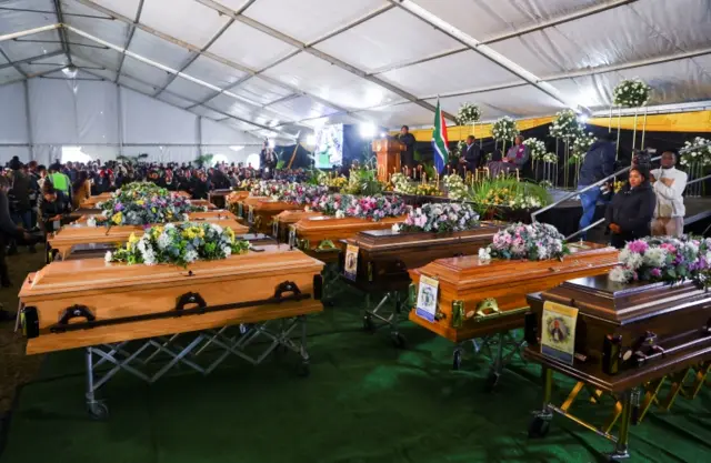 People gather near empty coffins ahead of a mass funeral for victims of an east coast tavern