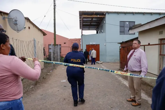 South African Police Services members use a tape to cordon off the entrance of a township pub in southern city of East London on July 5, 2022, after the death of 21 teenagers in the establishment