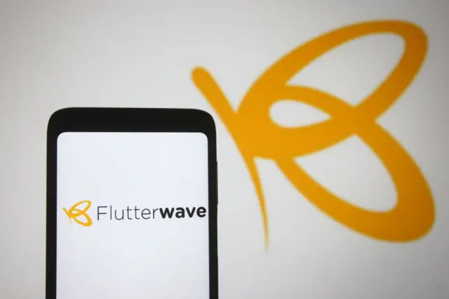 Flutterwave logo of a payments company is seen on a smartphone and a pc screen.