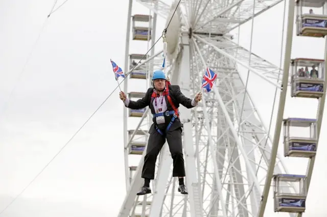 Johnson on a zipwire waving two Union flags during celebrations of the London 2012 Olympics