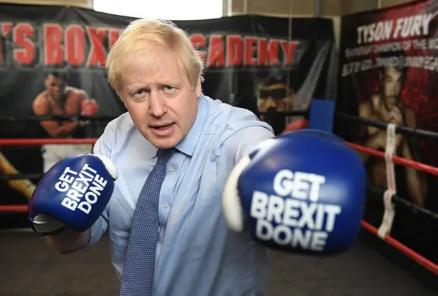 Boris Johnson in a boxing ring wearing gloves with the words Get Brexit Done written on them