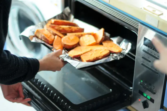 Sweet potatoes on a roasting tin being put into an oven