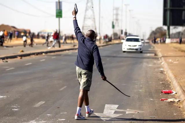 A man fires a hand gun in the air to disperse a mob of alleged looters outside of the Chris Hani Mall in Vosloorus, on July 14, 2021.