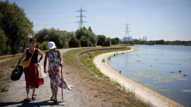 Two people walk along a water reservoir with low water levels in Walthamstow, London