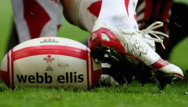 A rugby player's foot attempts to kick the ball