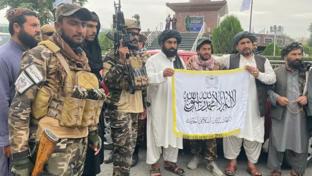 Taliban members pose with a flag in Kabul