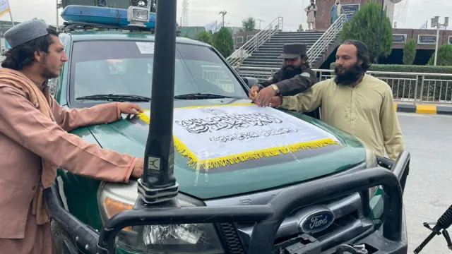 Taliban members gather beside a truck with a flag draped on top