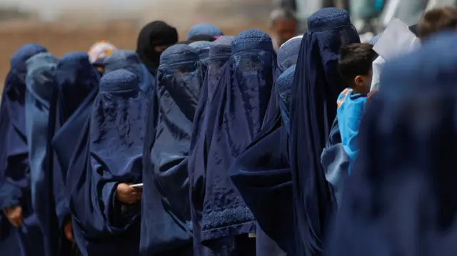 Afghan women wearing burkas stand in a queue for cash aid