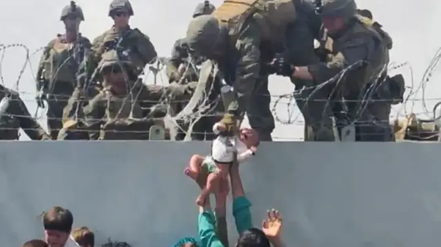 American soldiers on top of the Airport perimeter wall are handed a baby, Kabul, 19 Aug 2021