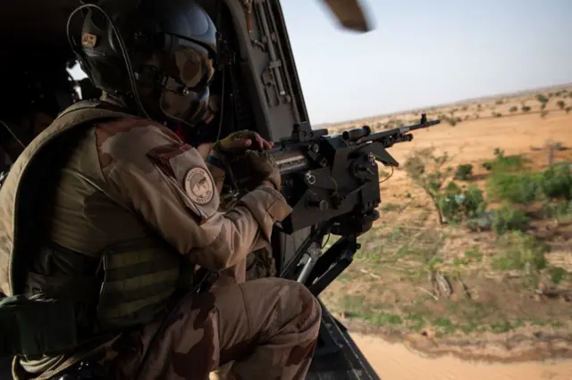 A soldier of the Barkhane force holds a weapon in an helicopter as he flies near a military base, on July 15, 2022