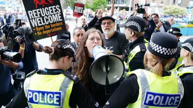 A woman carrying a loudspeaker is held back by police officers outside the hustings