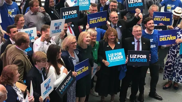 Liz Truss standing with supporters carrying Liz for Leader banners