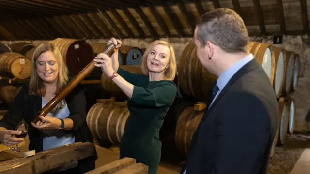 Liz Truss smiles as she extracts whiskey from a barrel