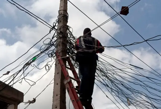 A technician with electricity distribution company stands on ladder and repairs a faulty line in Lagos, on September 29, 2020