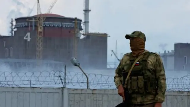 A serviceman with a Russian flag on his uniform stands guard near the Zaporizhzhia Nuclear Power Plant