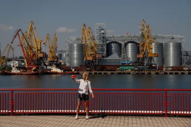 A woman takes a selfie with a grain terminal in a background in the sea port in Odesa after restarting grain export on 19 August 2022