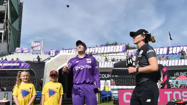 The toss is conducted by Kate Cross and Hollie Armitage